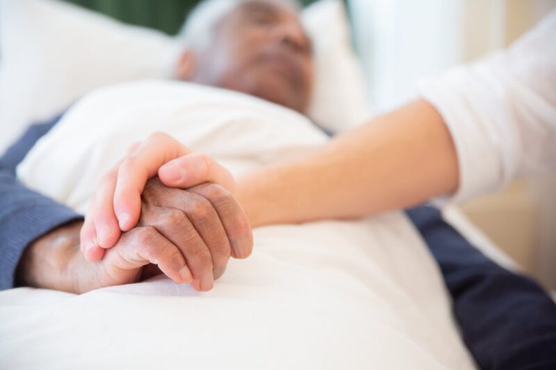 Caretaker Holding Patient's Hand In Bed
