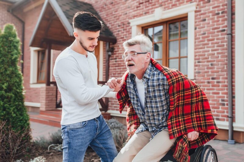 Young Man Helping Elderly Man From Wheelchair