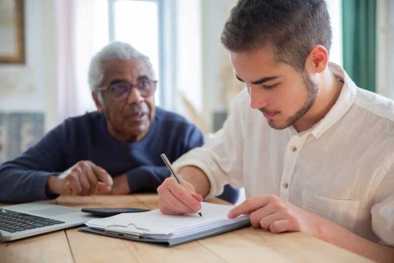 Young Man Helping Older Man With Paperwork