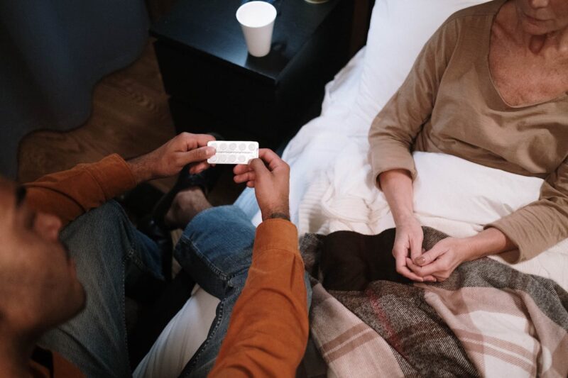 Man Giving Medication To Woman In Bed
